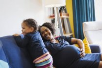 Giocosa incinta madre e figlia su divano — Foto stock
