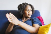 Щаслива вагітна жінка потирає руки разом на дивані — стокове фото