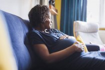 Ніжна вдумлива вагітна жінка, що розслабляється на дивані — стокове фото