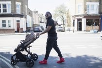 Ritratto felice padre spingendo bambino figlio in passeggino sulla soleggiata strada urbana — Foto stock