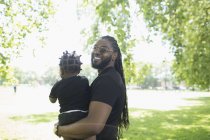 Porträt glücklicher Vater mit langen Zöpfen hält Kleinkind-Sohn im Park — Stockfoto