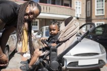 Portrait happy father with long braids and toddler son in stroller on sunny street — Stock Photo