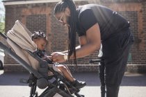 Father fastening toddler son in stroller on sunny sidewalk — Stock Photo