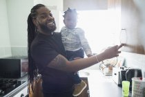 Portrait happy father holding toddler son in apartment kitchen — Stock Photo