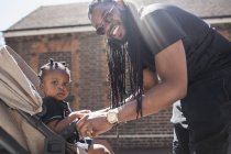 Portrait happy father with long braids fastening toddler son in stroller — Stock Photo