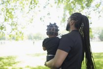 Pai com tranças longas carregando filho no parque — Fotografia de Stock