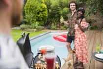 Happy young couple enjoying cocktails and barbecuing at poolside — Stock Photo