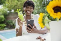 Feliz joven bebiendo cóctel y video chat en la piscina - foto de stock