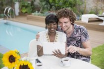 Feliz casal multiétnico usando tablet digital no pátio junto à piscina — Fotografia de Stock