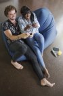 Jovem casal multiétnico jogando videogame em cadeira de saco de feijão — Fotografia de Stock