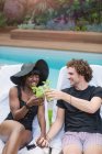 Счастливая молодая многонациональная пара пьет коктейли у бассейна — стоковое фото