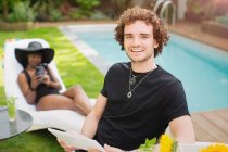 Portrait happy young man with digital tablet at poolside — Stock Photo