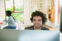 Молодой человек с наушниками работает за компьютером в домашнем офисе — стоковое фото