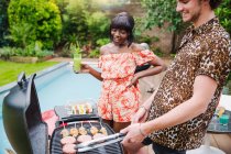 Young multiethnic couple barbecuing at poolside — Stock Photo
