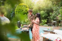 Young multiethnic couple barbecuing at summer poolside — Stock Photo