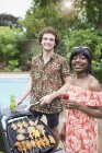 Portrait happy young multiethnic couple barbecuing at poolside — Stock Photo
