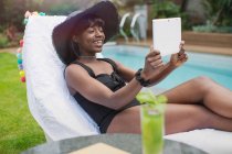 Heureuse jeune femme vidéo bavarder avec tablette numérique au bord de la piscine — Photo de stock