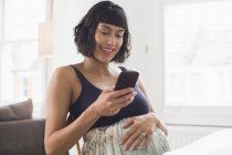 Donna incinta felice utilizzando smart phone — Foto stock