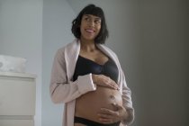 Happy pregnant woman in bathrobe and bra holding stomach — Stock Photo