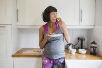 Happy pregnant woman eating in kitchen — Stock Photo