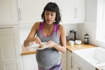 Mujer embarazada comiendo en la cocina - foto de stock