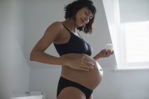 Donna incinta in reggiseno e mutandine applicando idratante allo stomaco — Foto stock