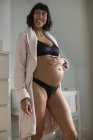 Mujer embarazada feliz en sujetador y bragas sosteniendo el estómago - foto de stock