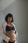 Pregnant woman in bra holding stomach — Stock Photo