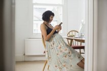 Вагітна жінка у квітковій сукні за допомогою смартфона за столом — стокове фото