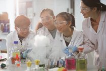 Professora e alunas assistindo a experimentos científicos reação química em sala de aula de laboratório — Fotografia de Stock