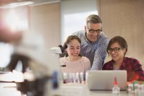 Чоловічий вчитель і студенти-дівчата проводять науковий експеримент в мікроскопі і ноутбуці в лабораторному класі — стокове фото