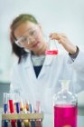 Girl student examining pink liquid, conducting scientific experiment in laboratory classroom — Stock Photo