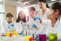 Female teacher and students conducting scientific experiment, watching liquid in test tube in laboratory classroom — Stock Photo
