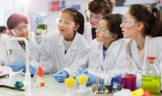Curious students conducting scientific experiment, examining liquid in beaker in laboratory classroom — Stock Photo