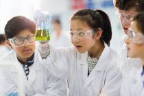 Curious students examining liquid in beaker, conducting scientific experiment in laboratory classroom — Stock Photo