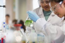 Студенти-дівчата проводять науковий експеримент, вивчаючи рідину в склянці в лабораторному класі — стокове фото