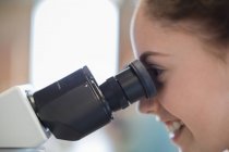 Close up perfil chica estudiante usando microscopio, realización de experimento científico - foto de stock