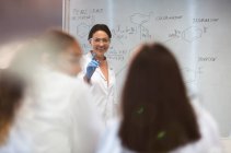 Sorrindo professor de ciências do sexo feminino lição de liderança no quadro branco em sala de aula — Fotografia de Stock