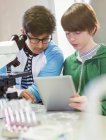 Focused boy students using digital tablet and microscope, conducting scientific experiment in laboratory classroom — Stock Photo