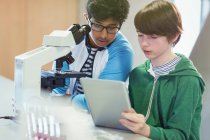 Focused boy students using digital tablet at microscope in laboratory classroom — Stock Photo