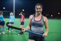 Portrait confident female field hockey player holding hockey stick on field — Stock Photo