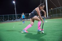 Focused young female field hockey player playing on field at night — Stock Photo