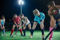 Focused young female field hockey players practicing sports drill on field at night — Stock Photo