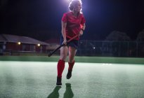 Giovane giocatore di hockey su prato femminile in esecuzione con bastone da hockey sul campo di notte — Foto stock