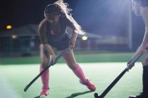Giovane giocatore di hockey su prato femminile determinata raggiungendo con bastone da hockey, giocando sul campo di notte — Foto stock