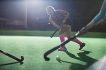 Young female field hockey running with hockey stick on field at night — Stock Photo