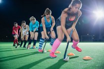 Determined female field hockey players practicing sports drill on field at night — Stock Photo
