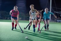 Junge Hockeyspielerinnen rennen um den Ball und spielen nachts auf dem Feld — Stockfoto