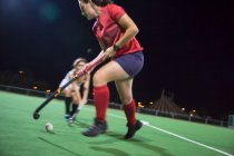 Young female field hockey players running for the ball, playing on field at night — Stock Photo