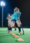 Determined young female field hockey player practicing sports drill on field at night — Stock Photo